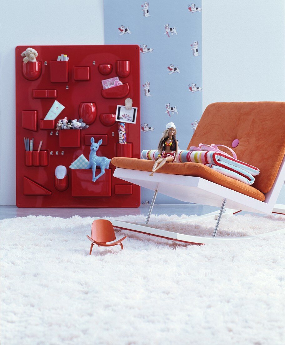 Moderner Schaukelstuhl vor rotem Utensilo mit Spielsachen