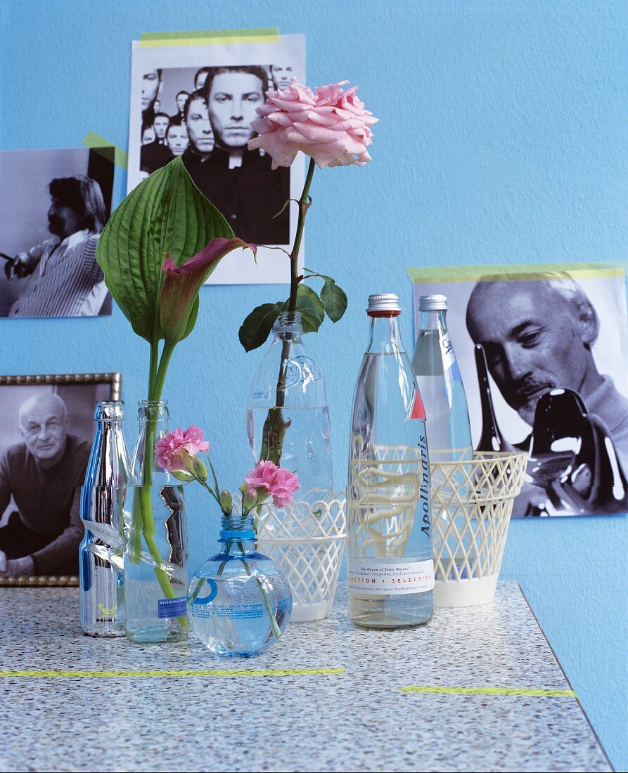 Water bottles used as vases in front of photos on blue wall