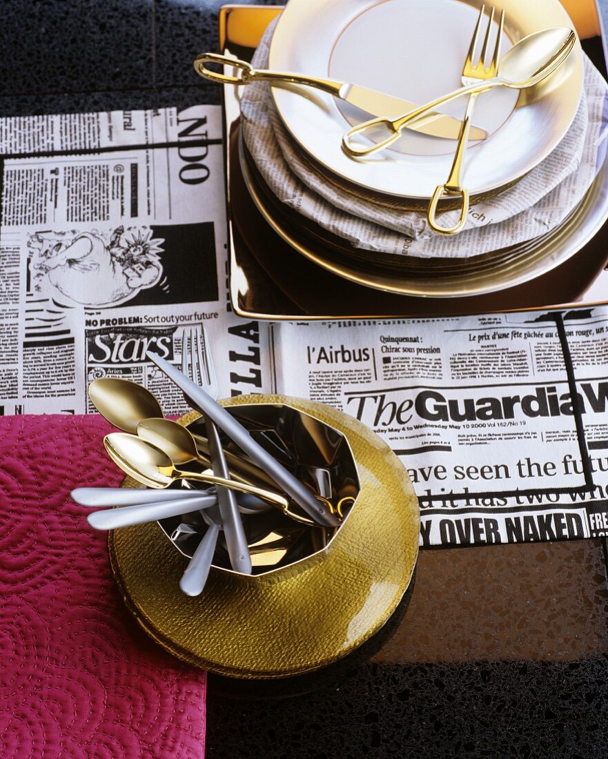 Geschirr und Besteck in Gold auf Zeitungspapier