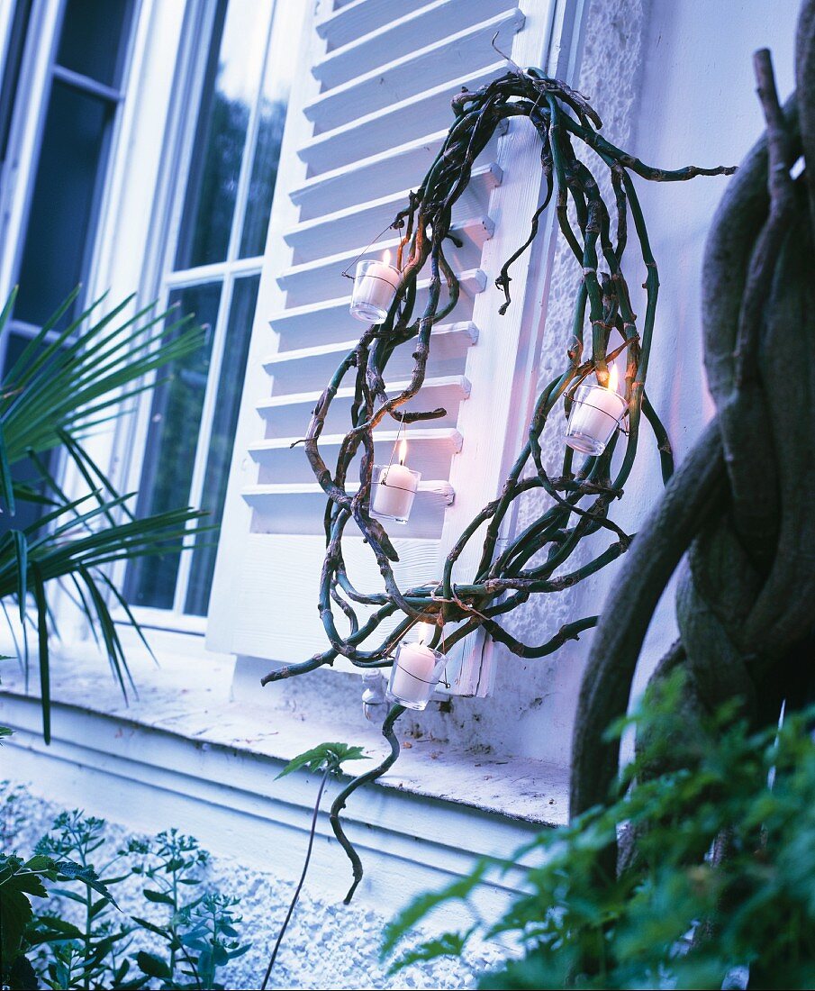 Kranz aus Zweigen mit Windlichtern am Fensterladen