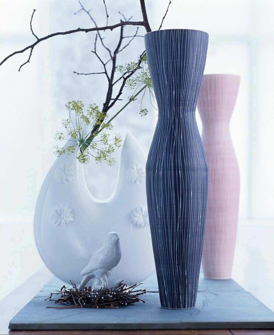 Drei Vasen mit Zweigen und ein Porzellanvögelchen im Dekonest