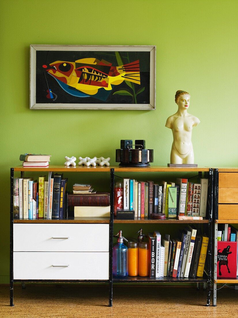 Sideboard-Regal mit weißen Schubladen und Büchern vor hellgrüner Wand mit gerahmter Kunst