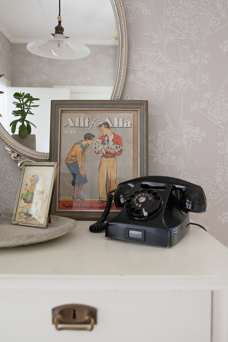 Old black telephone and vintage pictures on chest of drawers