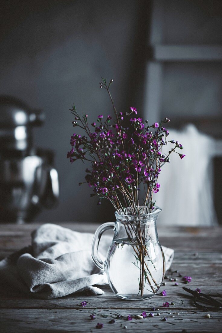 Blütenzweige in Glaskrug auf rustikalem Tisch in Landhausküche