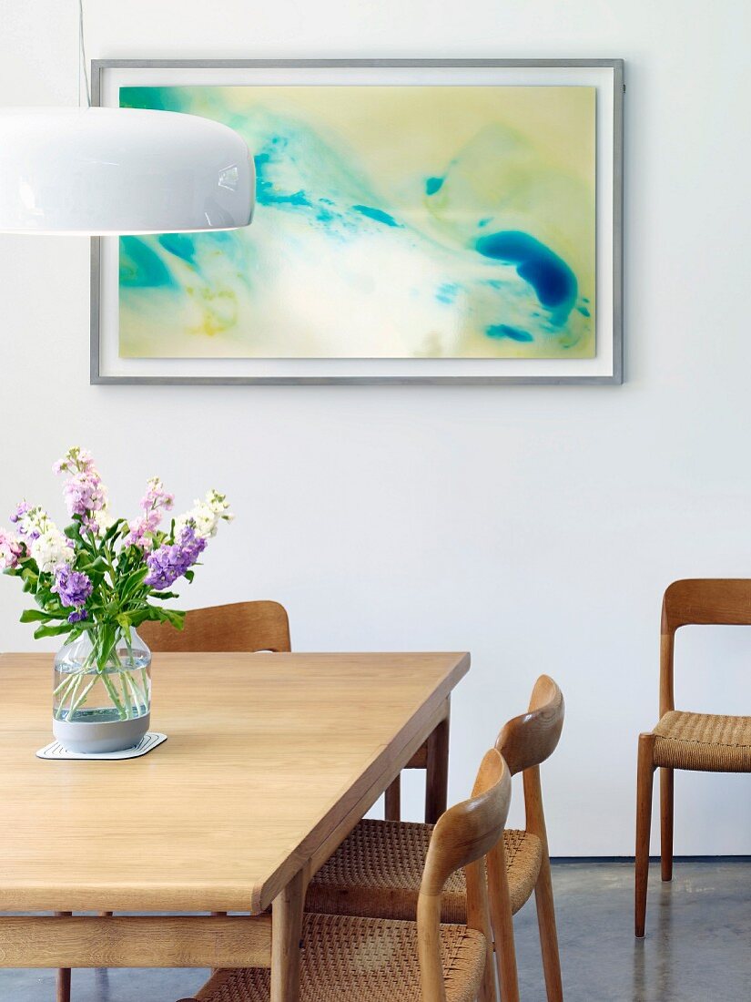 Wooden dining table and wood and cane chairs in front of modern painting