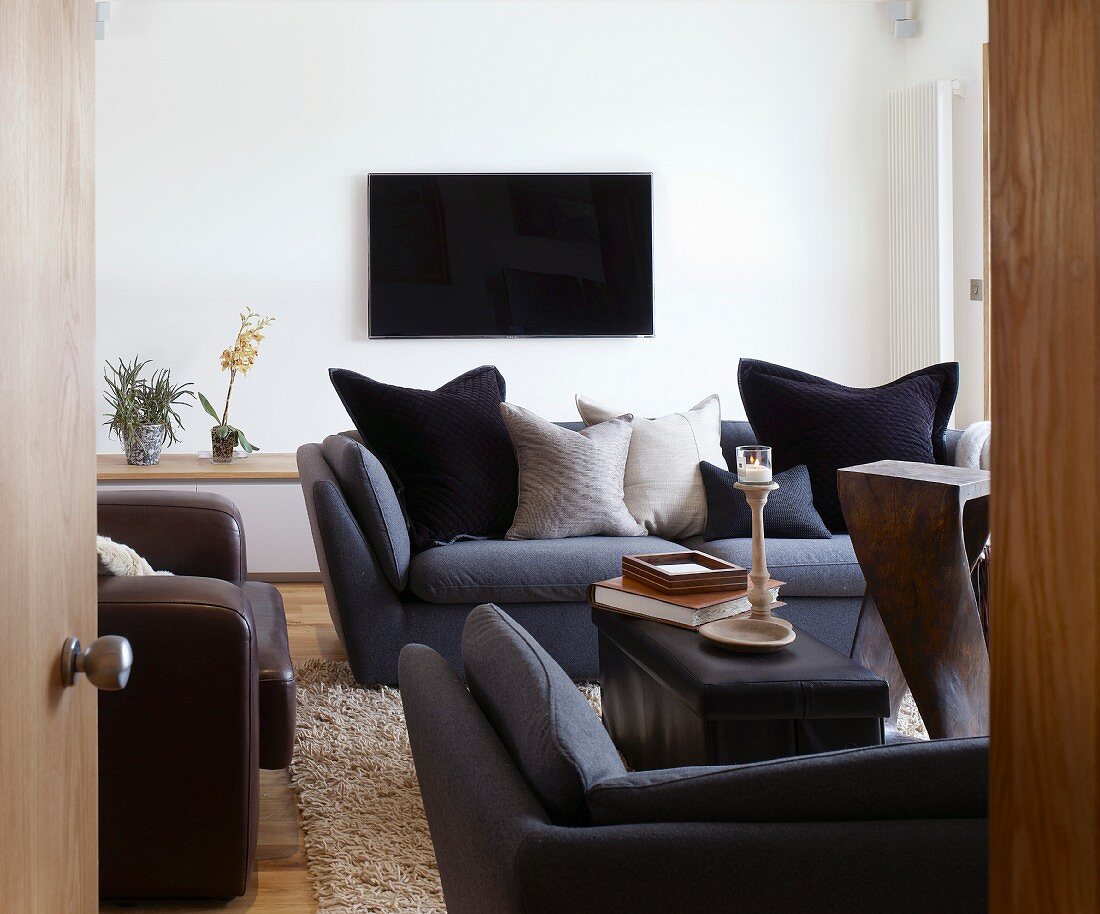Blick ins Wohnzimmer mit dunklen Polstermöbeln und Fernseher