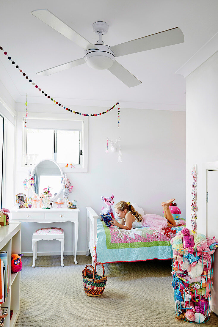 Weisses Kinderzimmer mit bunten Accessoires, Mädchen liegt mit Buch auf Bett