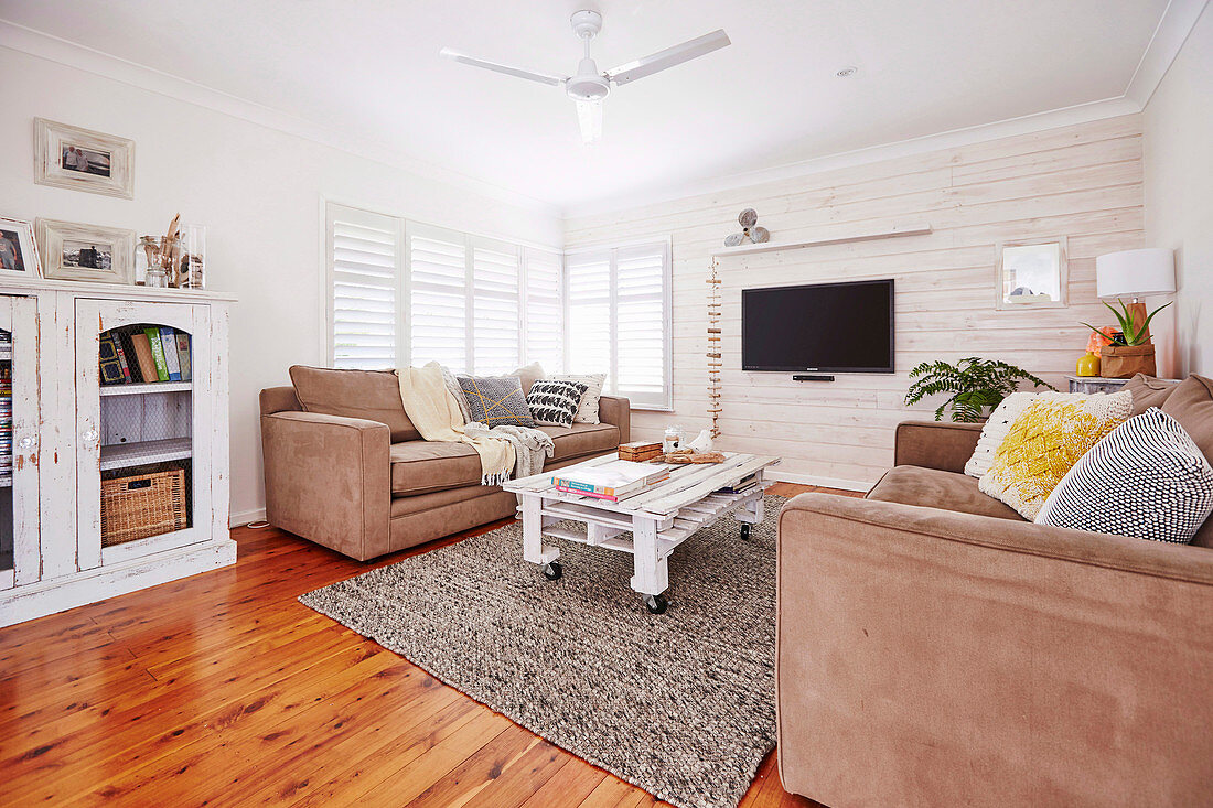 Upholstered set and rollable pallet table in the living room with white painted wooden wall