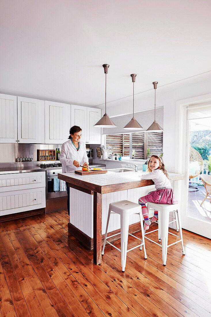 Mutter und Tochter in weisser, offener Küche mit Holzboden