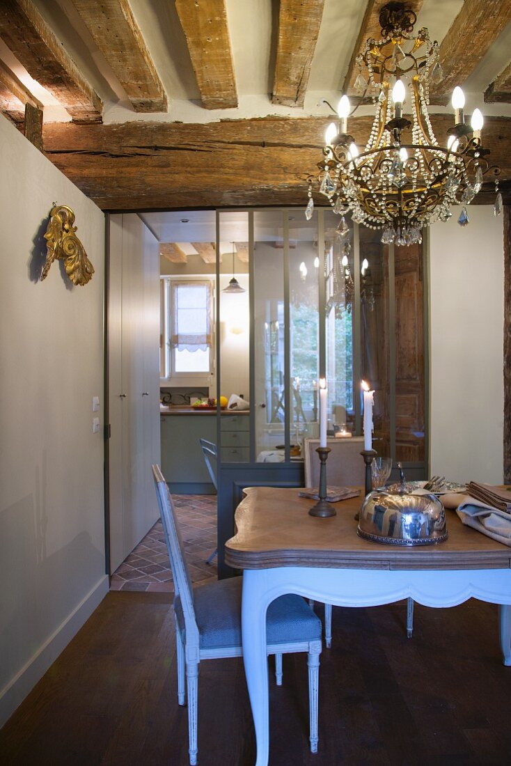 Chandelier, lit candles and rustic wood-beamed ceiling in dining area