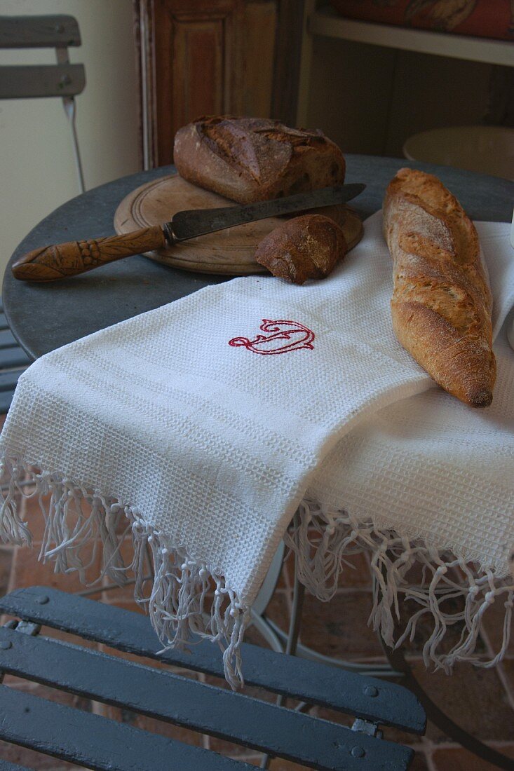 Bread knife, chopping board and bread on embroidered white cloth