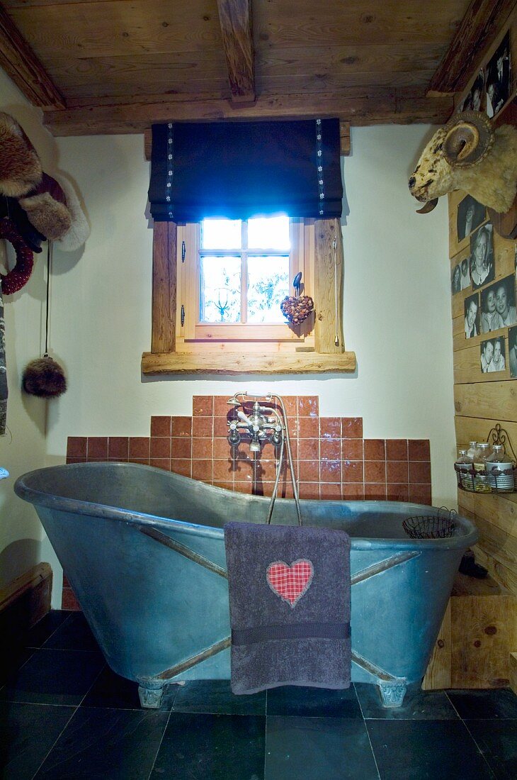 Heart motif on towel hung on vintage zinc bathtub below wooden window in chalet