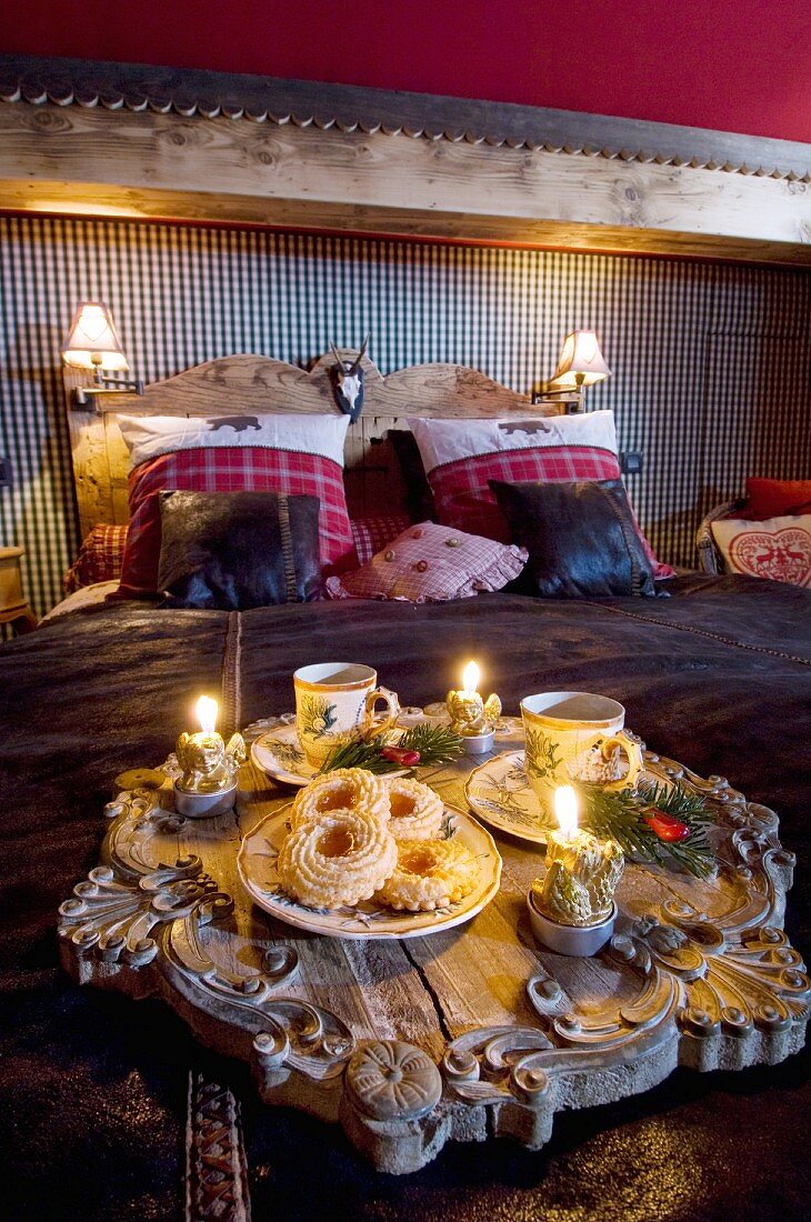 Antikes Holztablett mit Schnitzereien, Porzellan und weihnachtlichen Kerzen auf Bettdecke in Chalet-Schlafzimmer