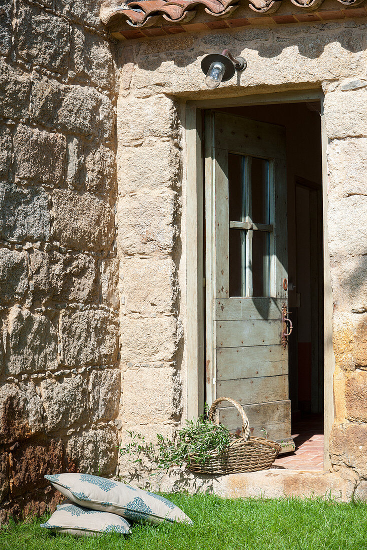 Kissen und Korb vor der offenen Tür eines rustikalen Steinhauses