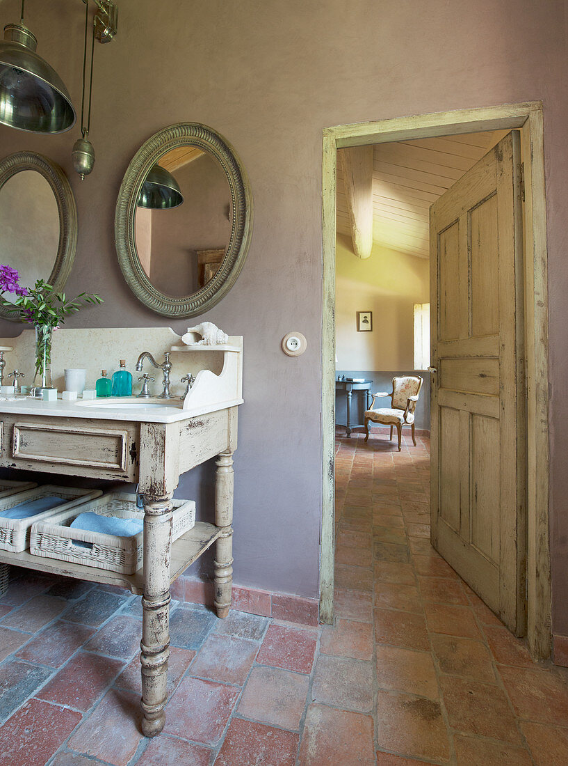 Offene Tür neben antikem Waschtisch mit ovalen Spiegeln