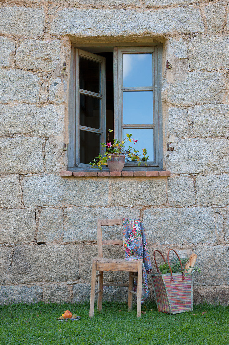 Old chair and shopping basket below open window of stone house