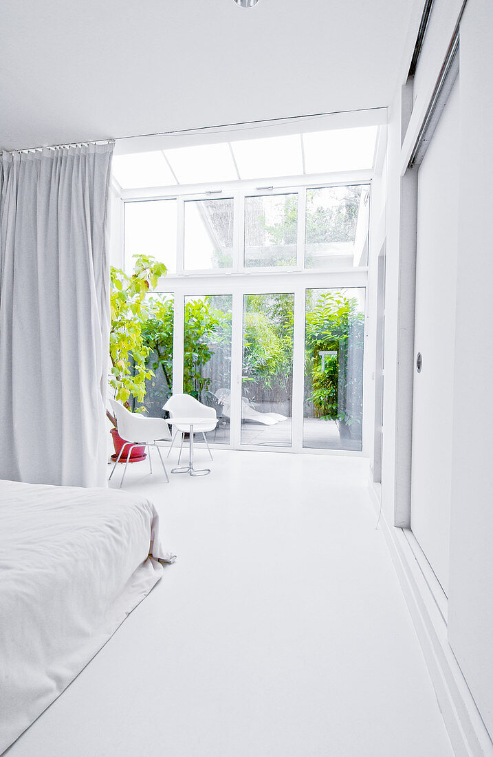 White bedroom with glass wall leading to conservatory