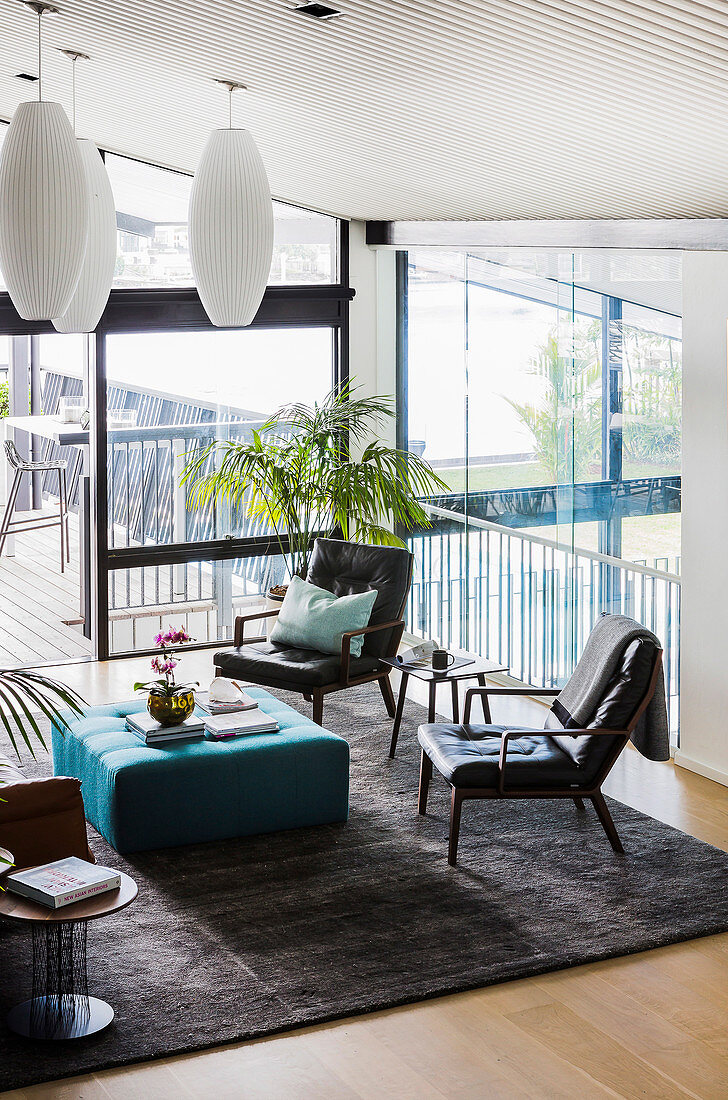 Lederstühle und türkisfarbener Polsterhocker auf Teppich in Lounge mit raumhohen Fenstern