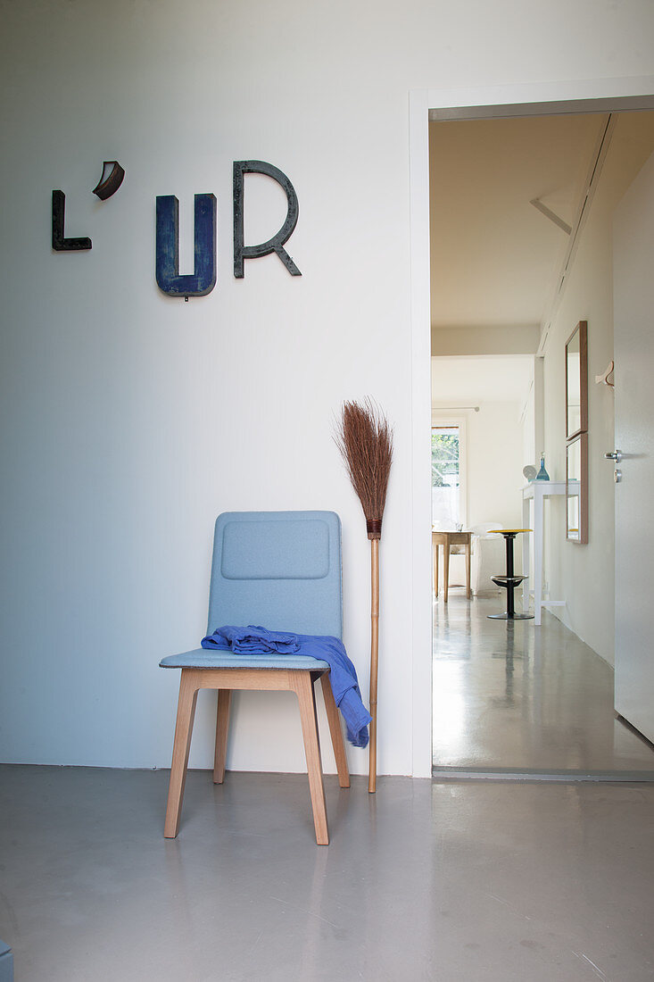 Reisigbesen und blauer Stuhl unter Dekobuchstaben neben der Tür