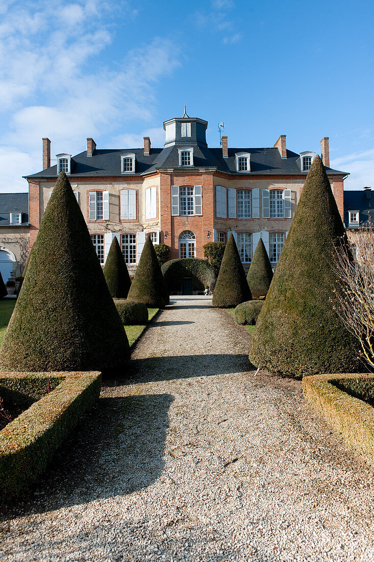 Blick auf das Château Les Aulnois aus dem Park mit kegelförmigen Hecken