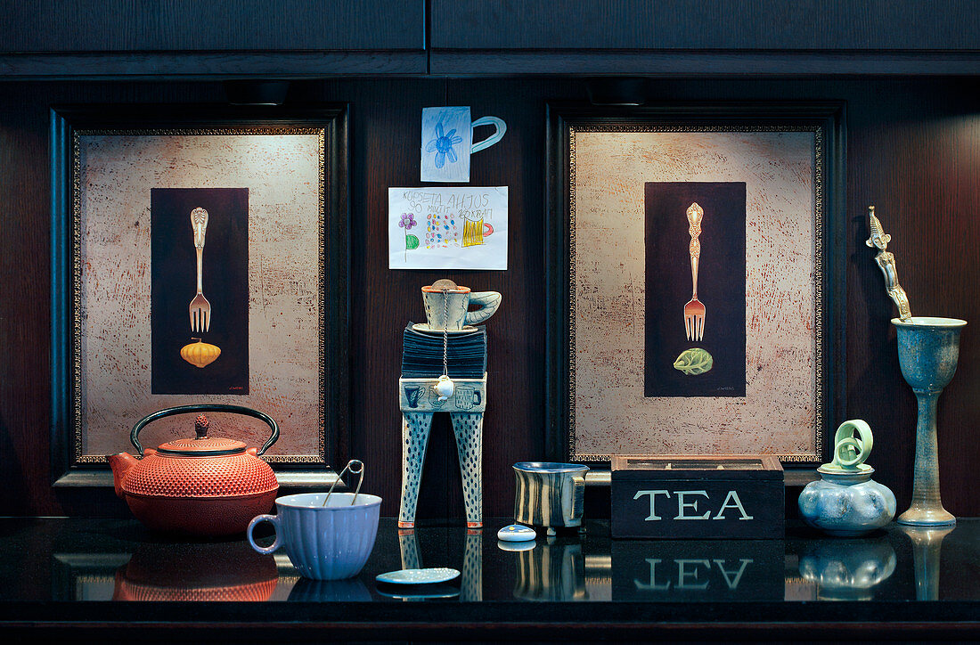 Teapot and cups in front of two illuminated pictures of forks
