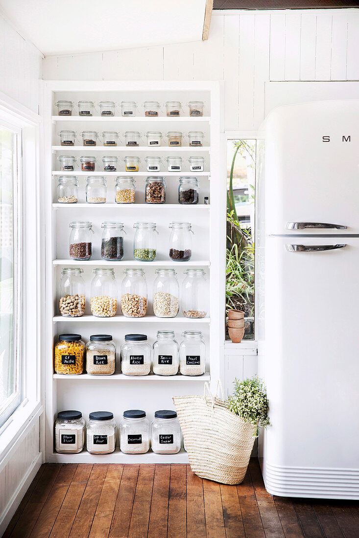 Open white shelf with storage jars next to fridge