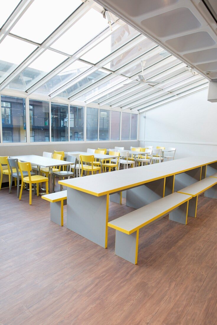 Tables, chairs and benches in grey and yellow under glass roof