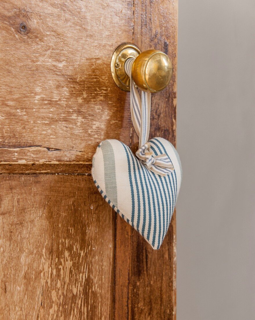Herz aus blau-weiß gestreiftem Stoff hängt am Knauf einer Holztür
