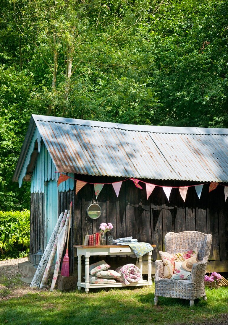 Holzhütte mit Wellblechdach im Garten, dekoriert mit bunter Stoff-Wimpelkette