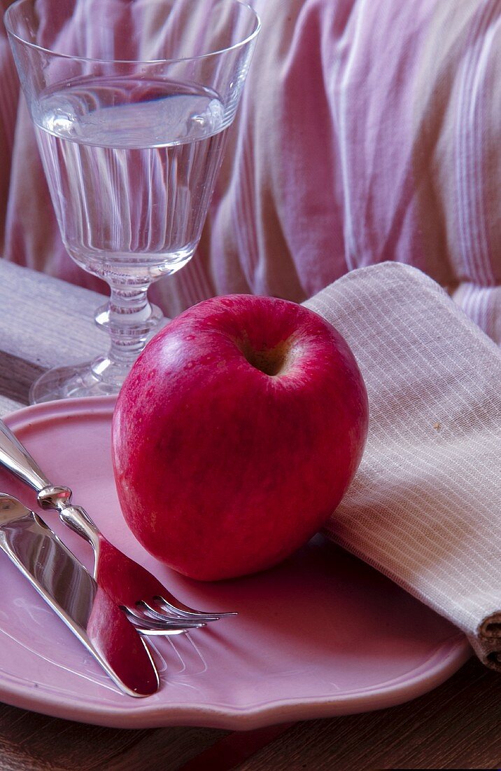 Pinker Apfel auf einem rosafarbenem Teller mit Besteck und Wasserglas
