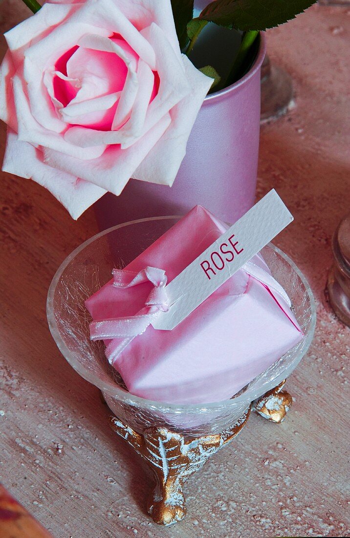 In rosafarbenem Papier verpackte Seife mit Etikett neben einer Rose