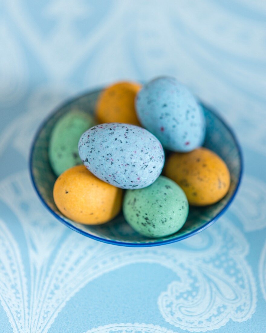 Bunte gesprenkelte Eier in Schale auf hellblauer Tischdecke