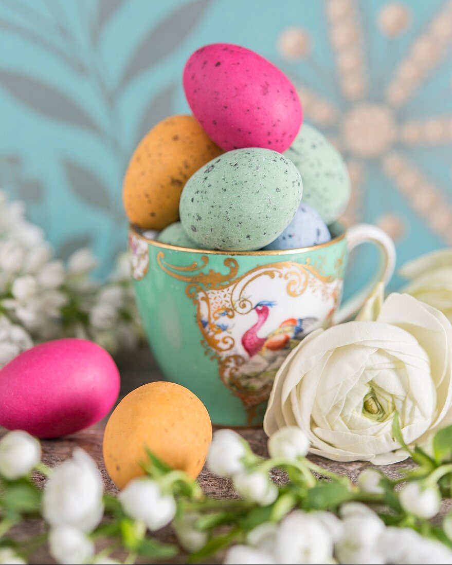 Colourful speckled eggs in vintage gold-rimmed teacup arranged with white flowers