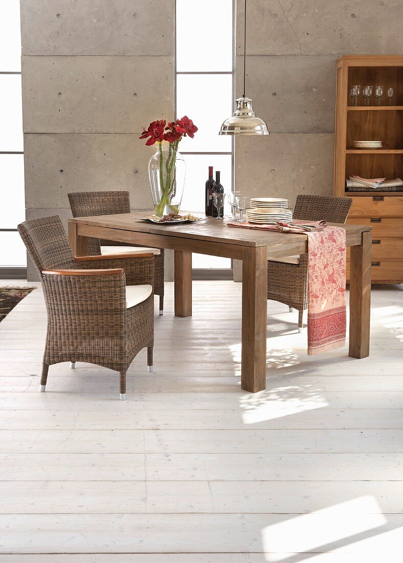 Elegant rattan armchairs and solid-wood table in front of concrete wall with vertical glazed stripes