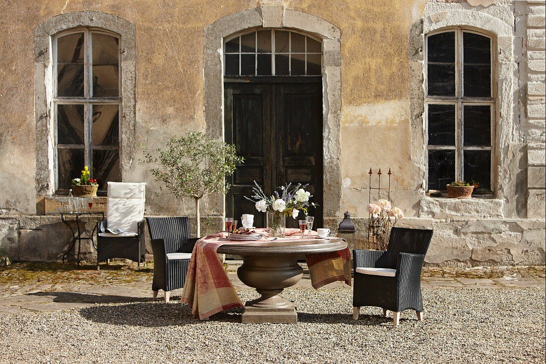 Massiver, runder Tisch und schwarze Outdoorsessel vor Vintage Landhaus