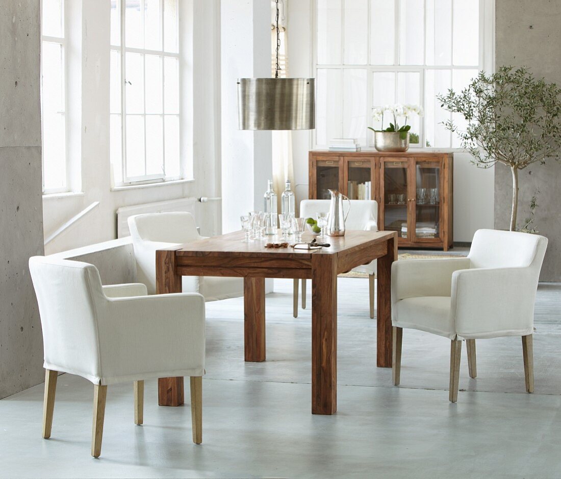 White armchairs and solid exotic-wood table in bright interior with industrial glazing