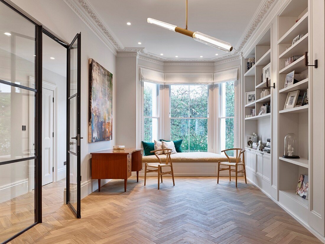 Fitted shelving, herringbone parquet and seating area in window bay in classic interior