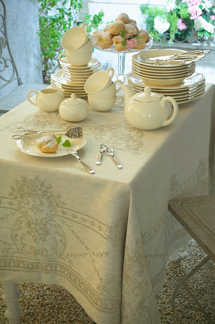 Staked china, tea service and pastries on elegant tablecloth on balcony table