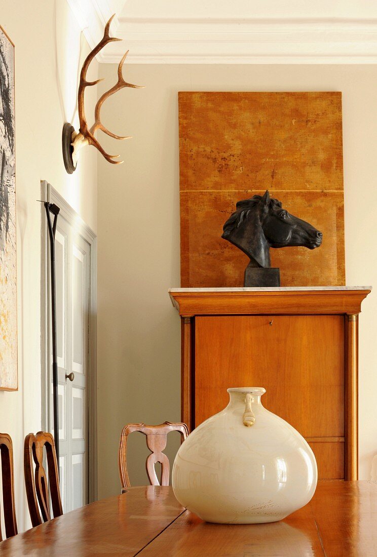 Edelholztisch mit Keramikgefäß vor Pferdekopf-Büste und Jagdtrophäe