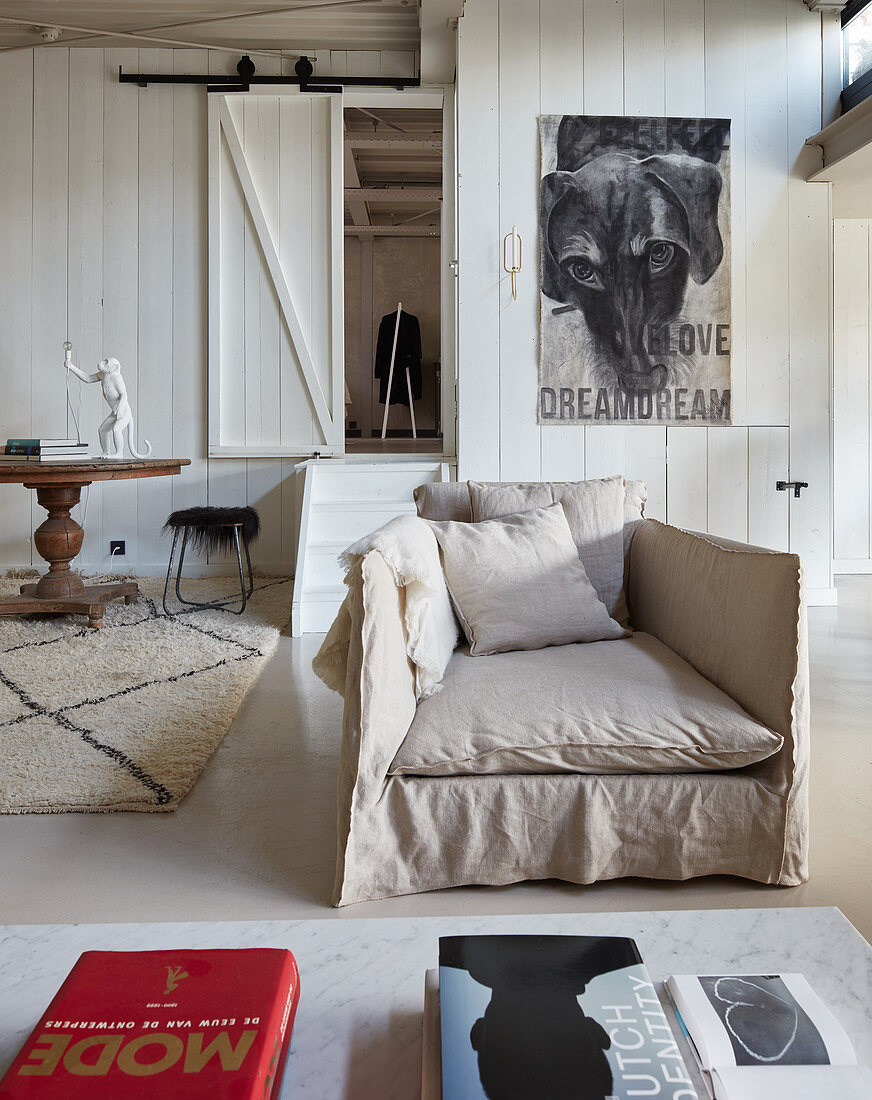 Loose-covered armchair against wood-clad wall and doorway leading to bedroom in loft apartment