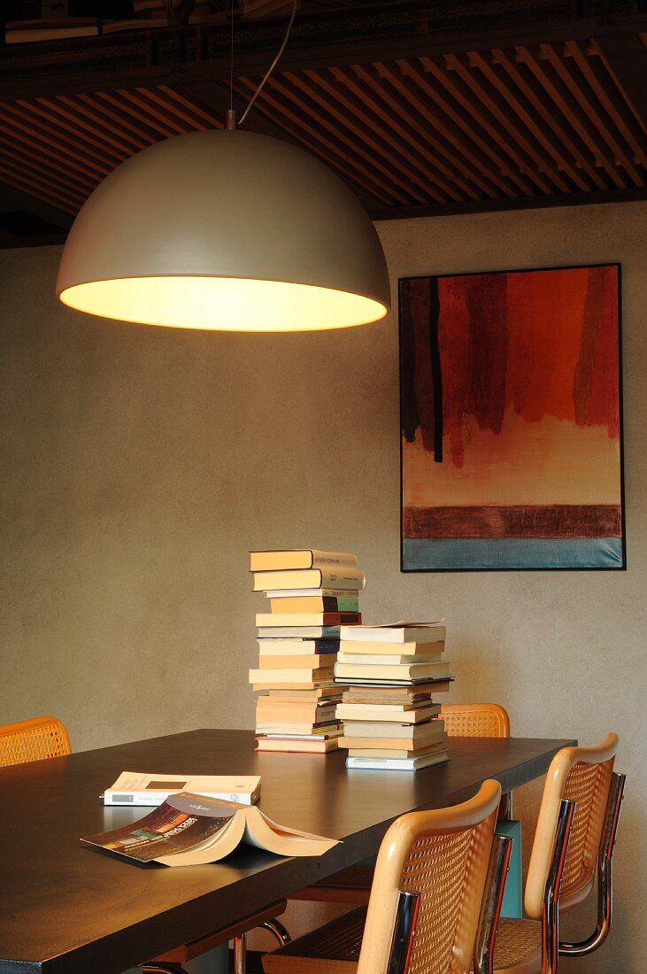 Large hemispherical lamp above stacked books on dining table