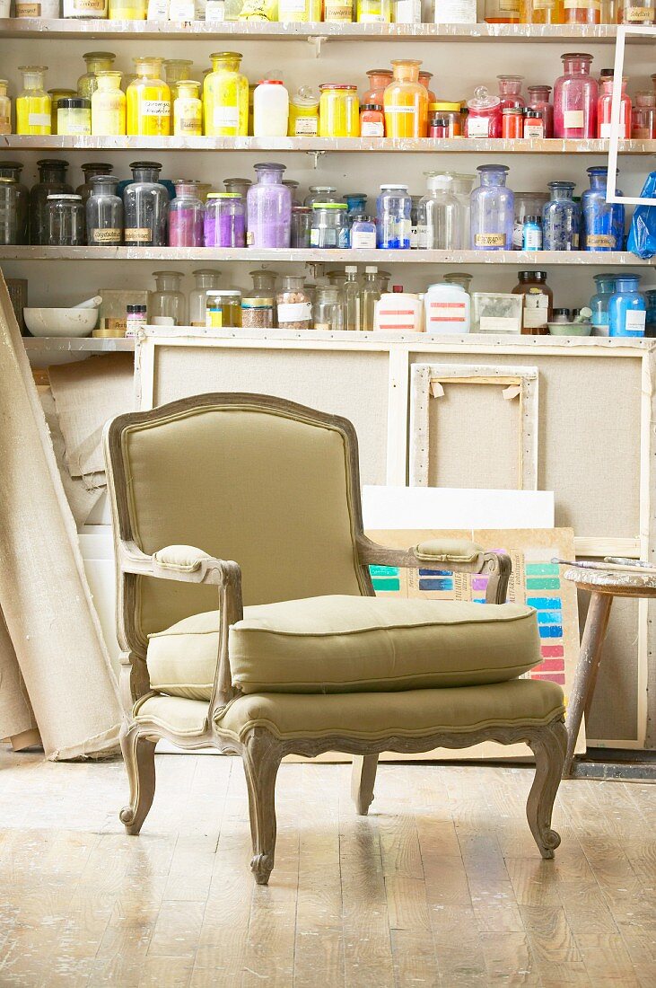French-style armchair in front of jars of pigments on shelves