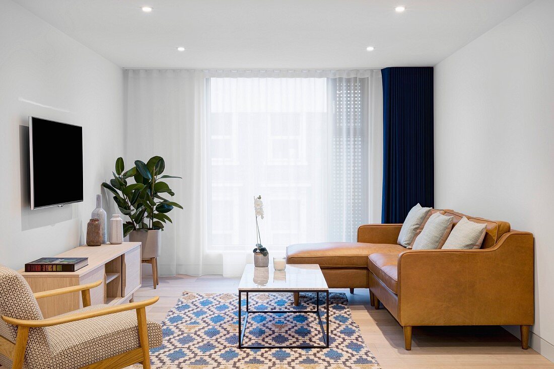 Loungebereich im Retro-Stil mit brauner Eckcouch, fligranem Couchtisch, Zimmerpflanze und Fernseher