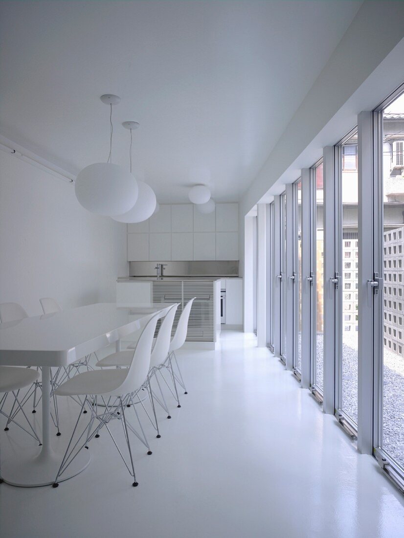 Weisser Essbereich mit langer Tisch und Klassikerstühlen vor Glastüren