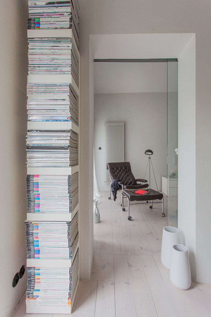 Vertikales Regal mit Zeitschriften vor dem Durchgang zu braunem Sessel