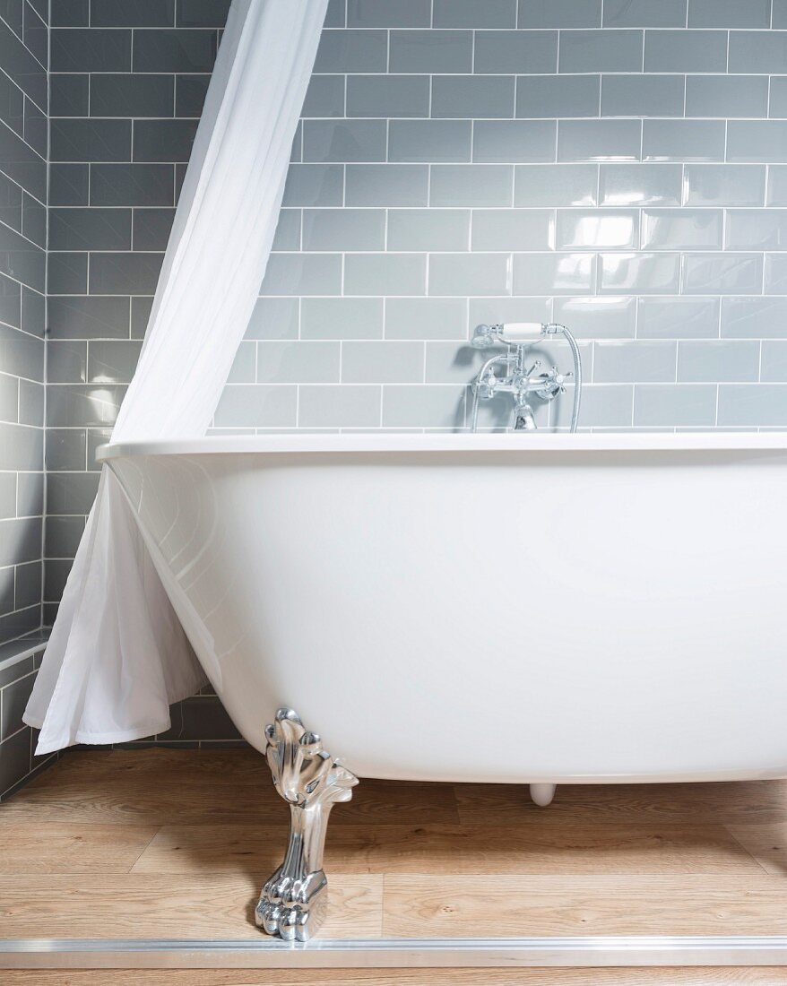 Free-standing bathtub with claw feet against grey wall tiles