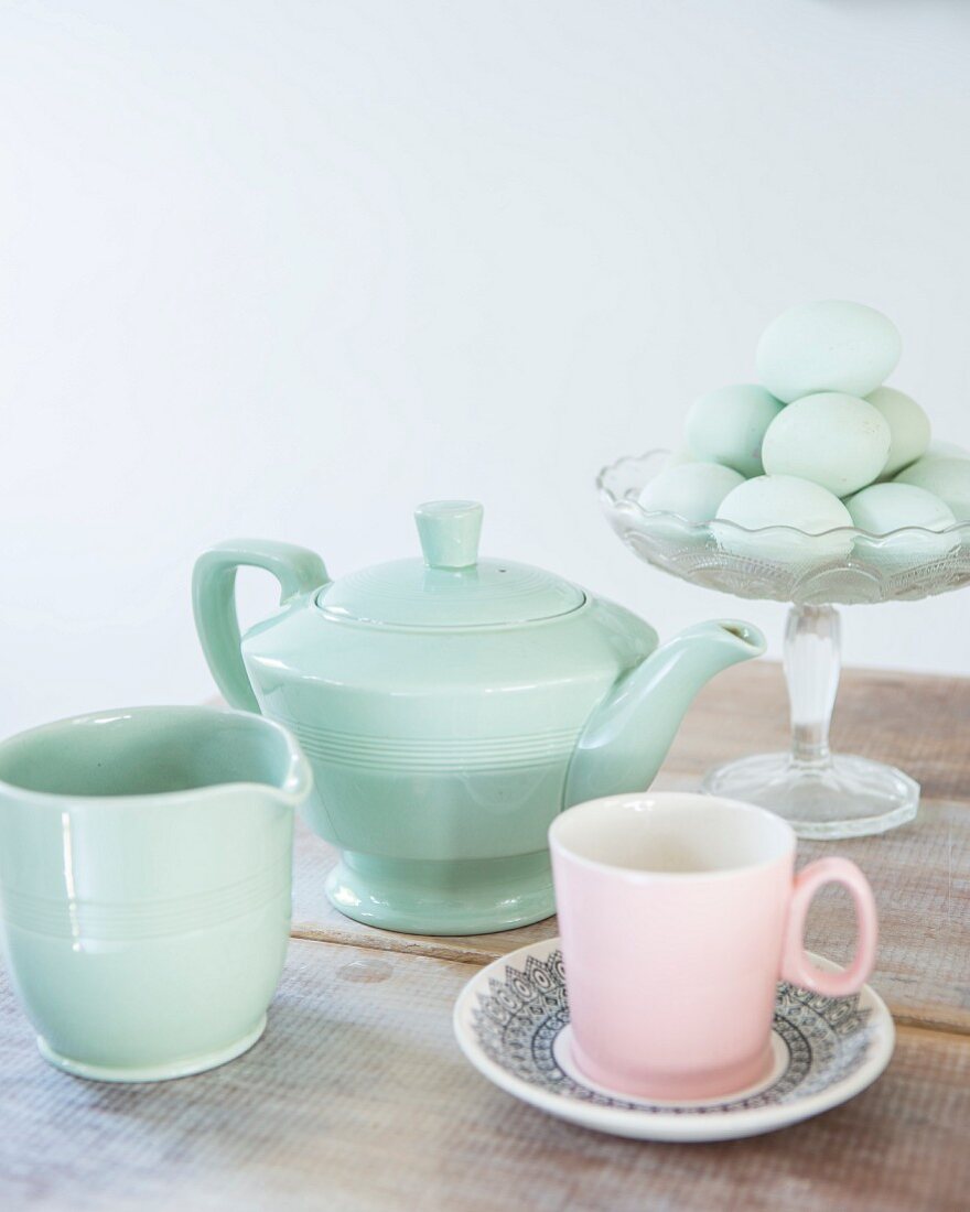 Retro Teekanne, Milchkännchen und rosafarbene Tasse vor Eiern in Glasschale