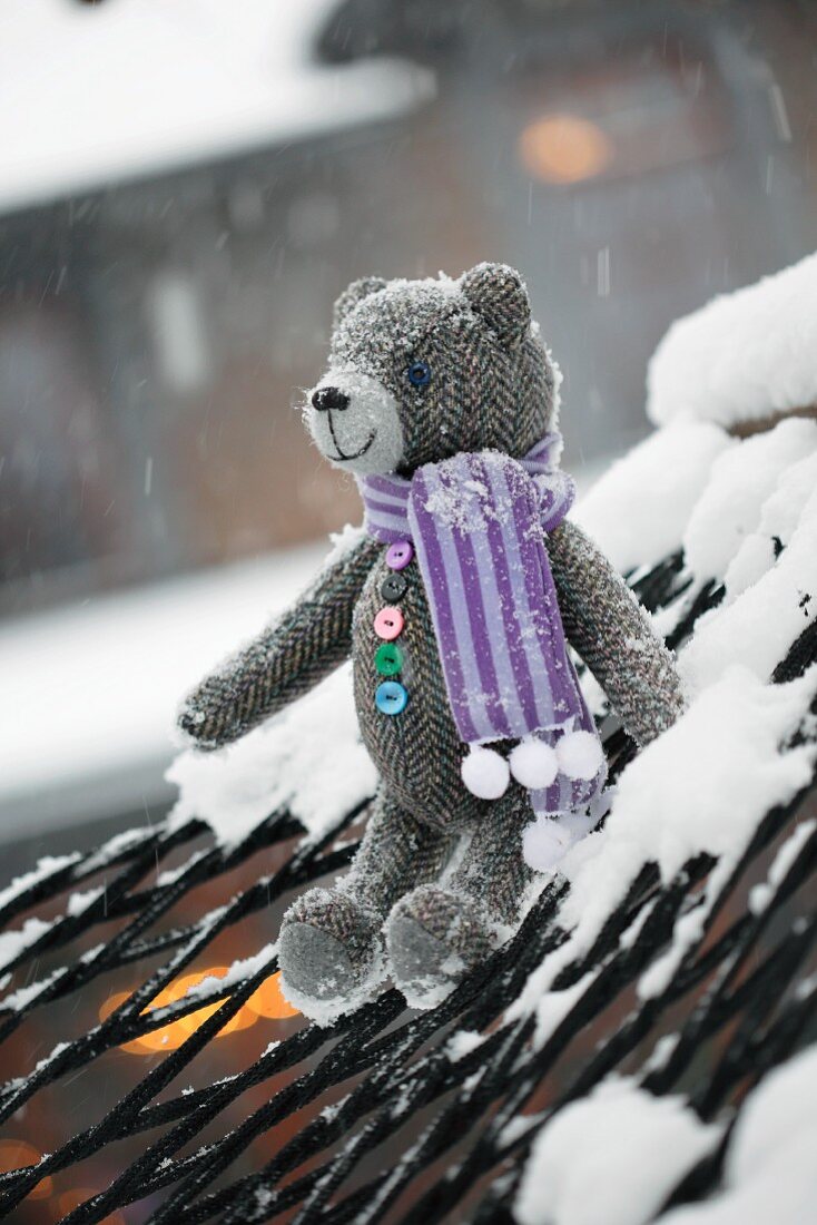 Teddybär aus Tweedstoff mit Schal auf verschneiter Hängematte