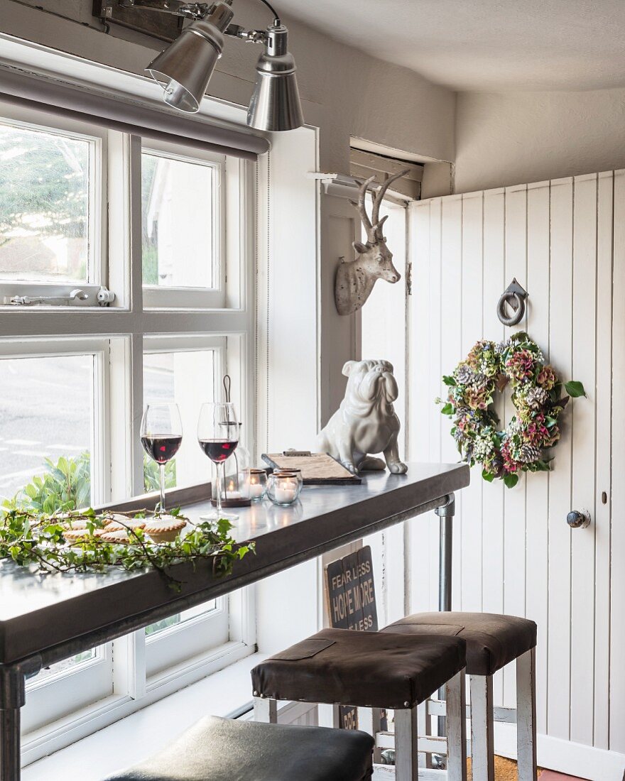 Wine glasses and dog ornaments on narrow table next to window next to open front door decorated with wreath