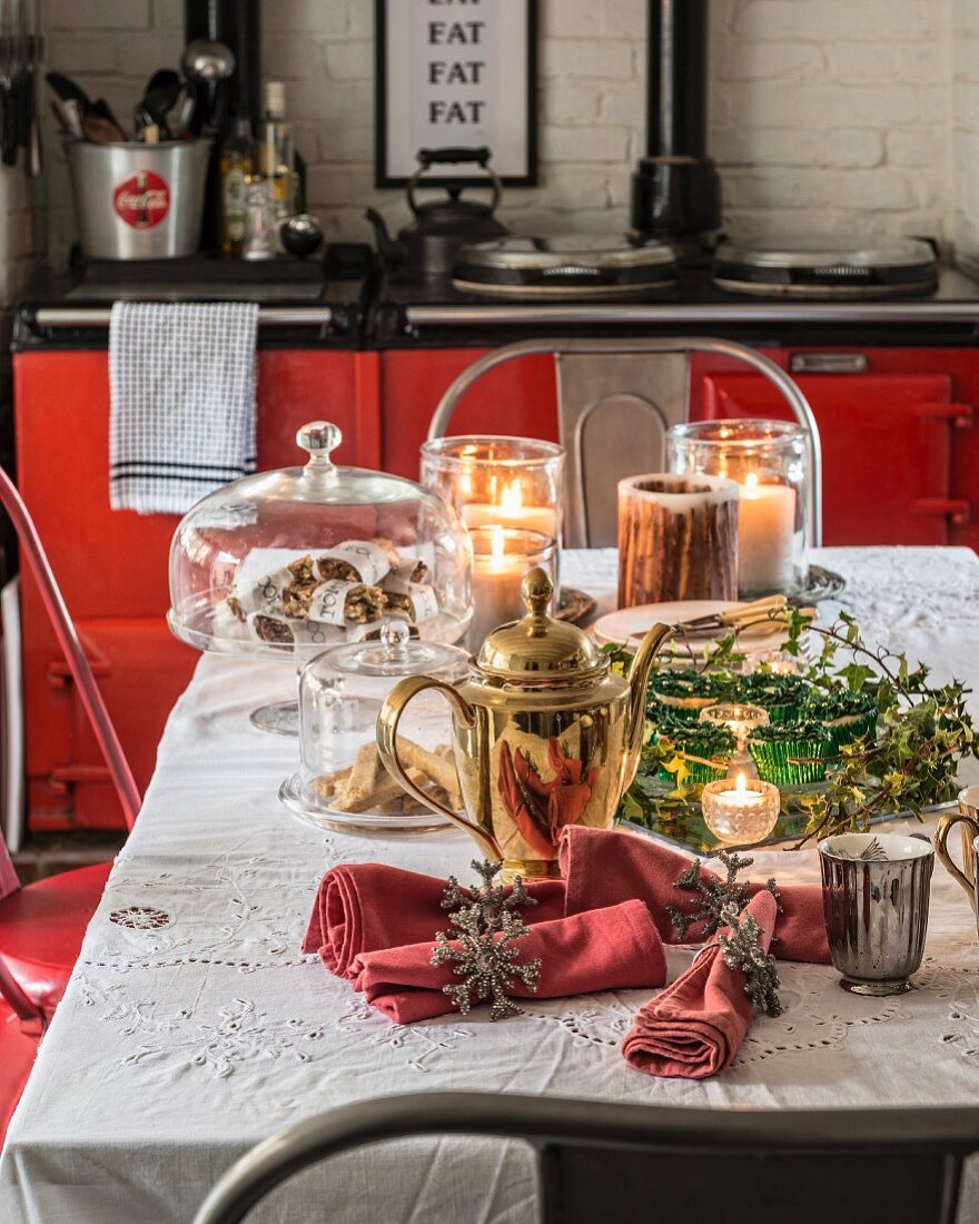 Weihnachtliche Tischdekoration mit goldglänzender Kanne und Kerzenlicht in Küche mit rotem Herd